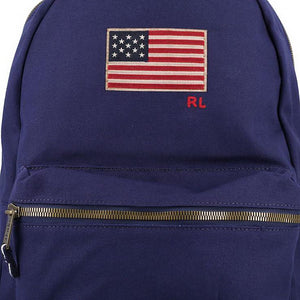 Close-up detail of the embroidered US flag patch, RL initials, and metallic brass zipper on an original Ralph Lauren navy blue backpack.
لقطة قريبة لمكعبات تطريز رقعة العلم الأمريكي وأحرف RL والسحاب النحاسي المعدني على حقيبة ظهر رالف لورين أصلية باللون الكحلي