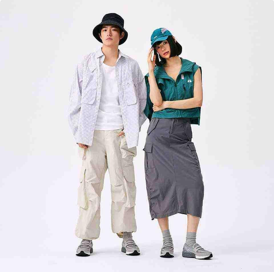 Male and female models stand side-by-side, each wearing a distinct outfit with the New Balance 1906L Grey sneakers, perfectly illustrating how the shoe serves new balance 1906l men and women (نيو بالانس 1906L رمادي للنساء والرجال).
