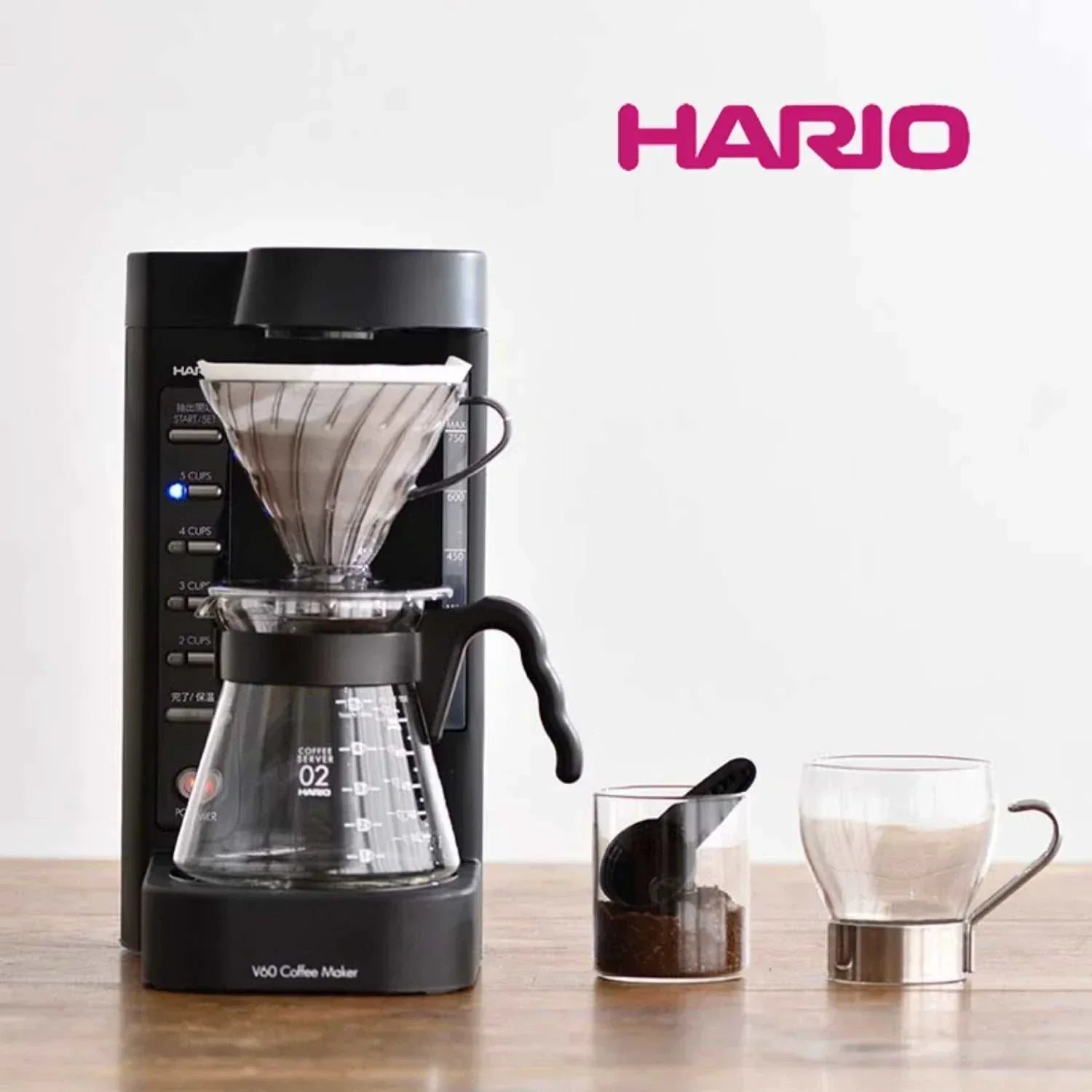 صانعة القهوة المفلترة الأوتوماتيكية Hario V60 باللون الأسود main setup view مع إبريق صب زجاجي وملحقات القياس.