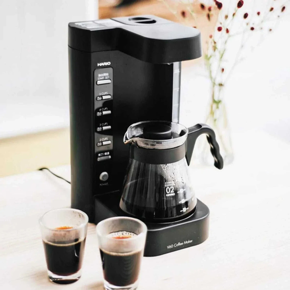 آلة قهوة Hario V60 المفلترة الأوتوماتيكية kitchen countertop setup مع كوبين زجاجيين للقهوة.